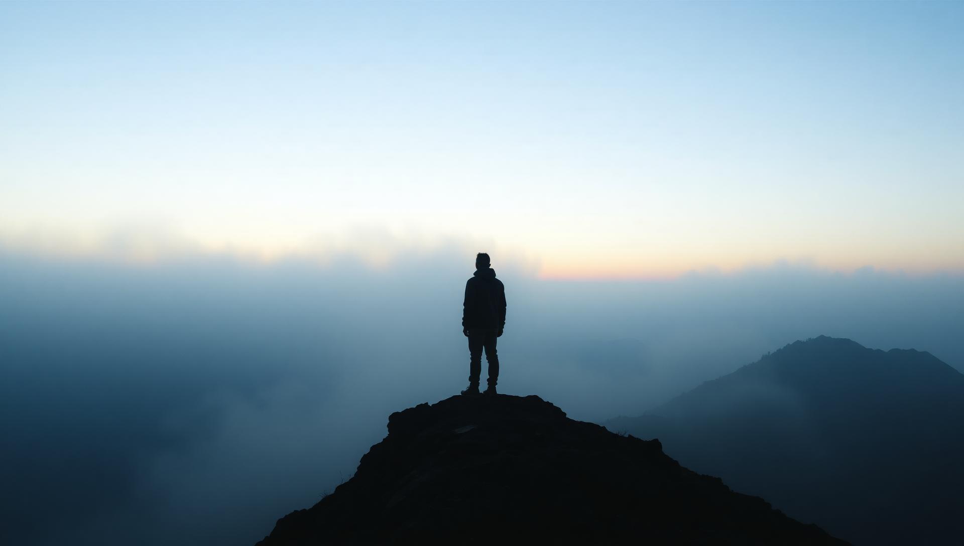 A lone figure on a misty mountain ridge at dawn